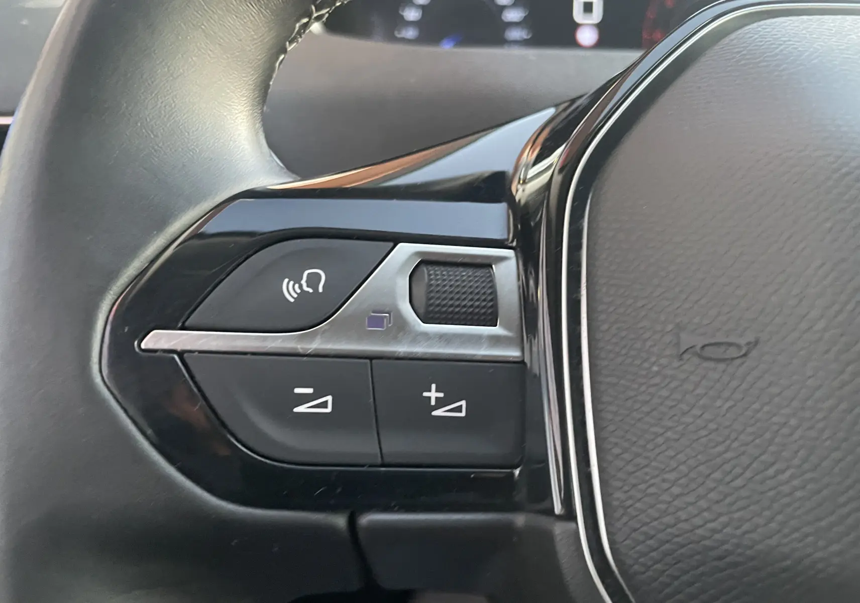 Gros plan sur les commandes du volant côté gauche du Peugeot 3008 blanc nacré, version 2019 avec boutons de volume et commande vocale.