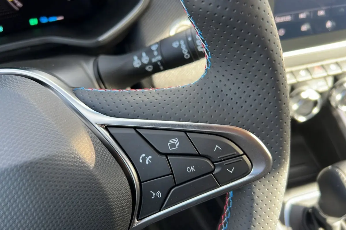 Gros plan sur les commandes du volant en cuir perforé noir avec surpiqûres tricolores de la Renault Clio V E-Tech 145 Esprit Alpine.