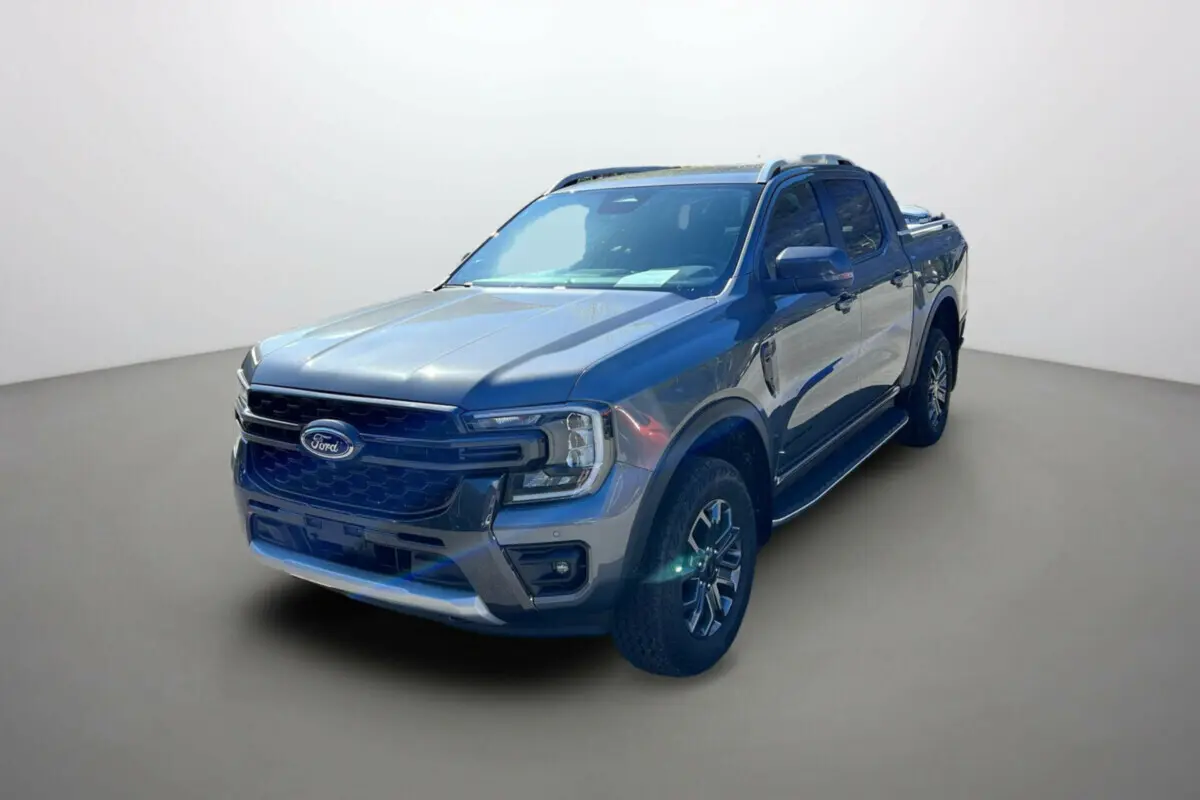 Ford Ranger 2026 gris carbone en 3/4 avant droit, avec jantes alu 18 pouces et barres de toit visibles.
