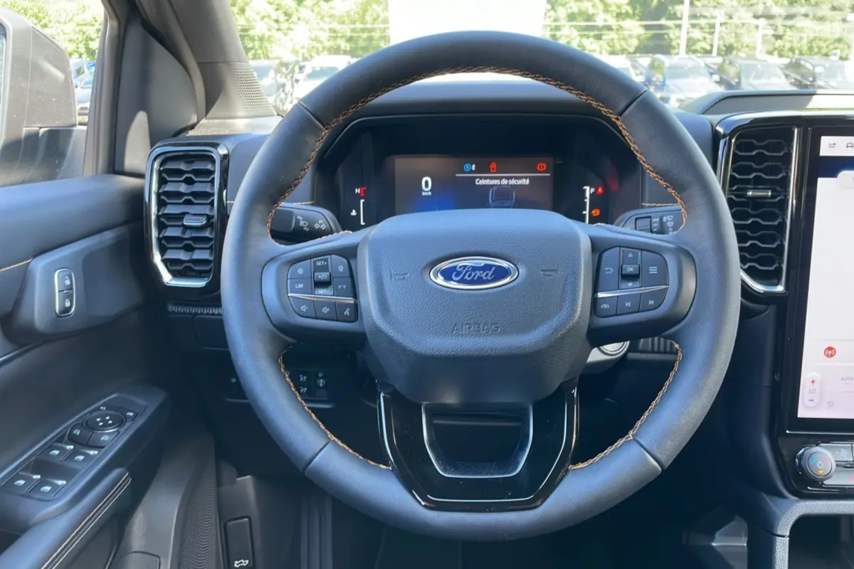 Vue rapprochée du volant cuir multifonctions du Ford Ranger gris carbone, avec tableau de bord numérique et commandes intégrées.