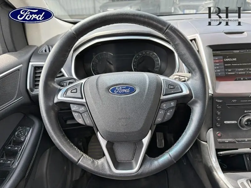 Vue rapprochée du volant cuir noir Ford Edge 2016 avec commandes intégrées et tableau de bord visible.