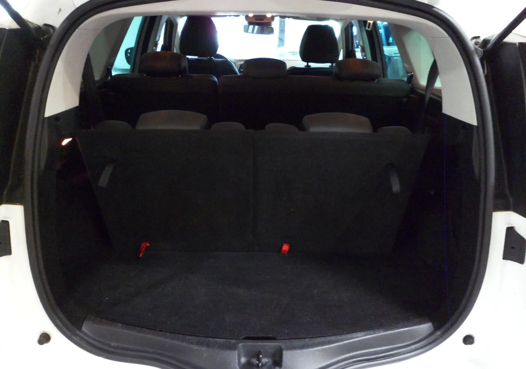 Coffre ouvert d'un Renault Grand Scenic IV blanc Glacier de 2019, montrant les sièges arrière et l'espace de chargement noir.