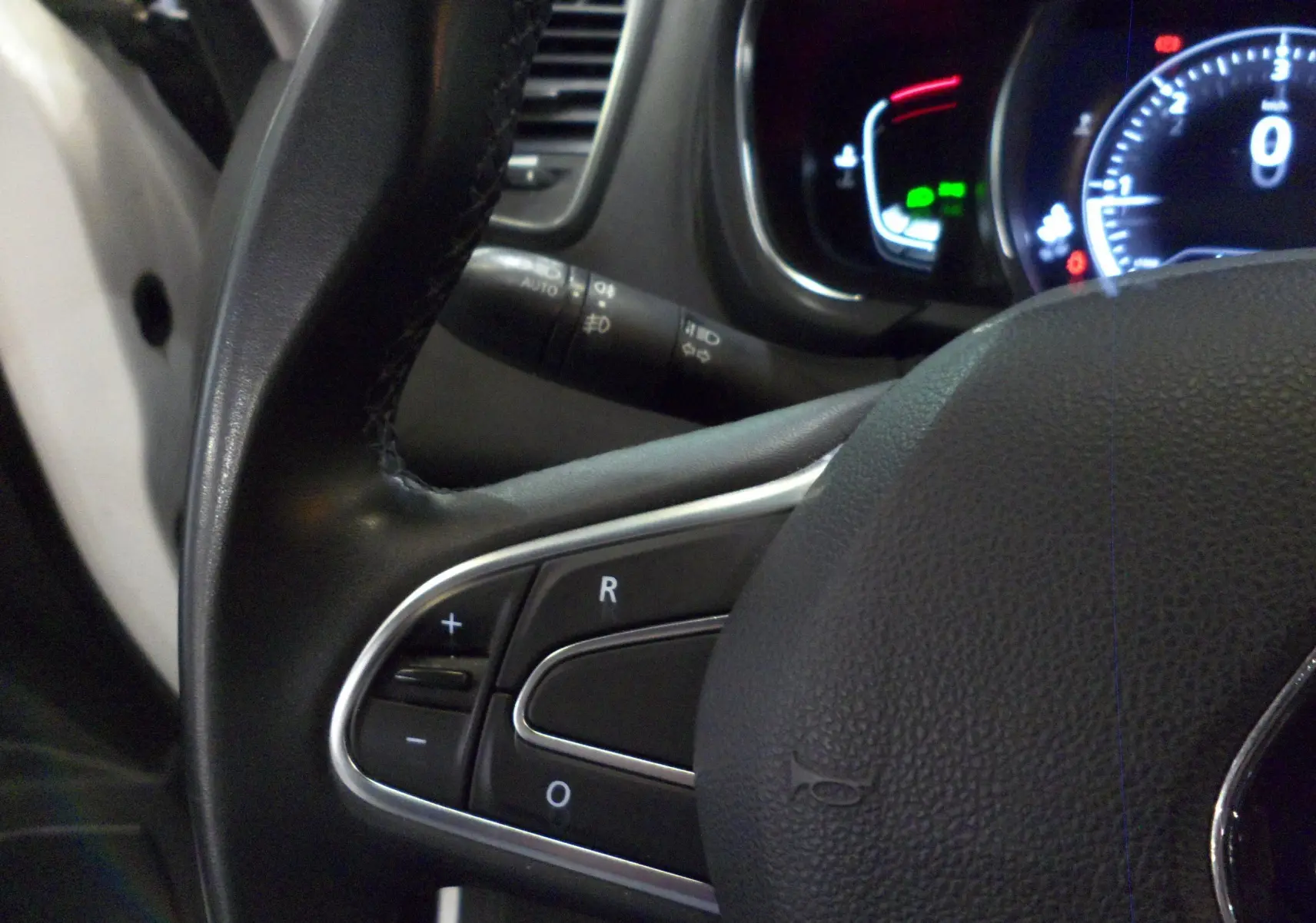 Gros plan sur le volant noir du Renault Grand Scenic IV blanc, avec commandes intégrées et tableau de bord lumineux en arrière-plan.