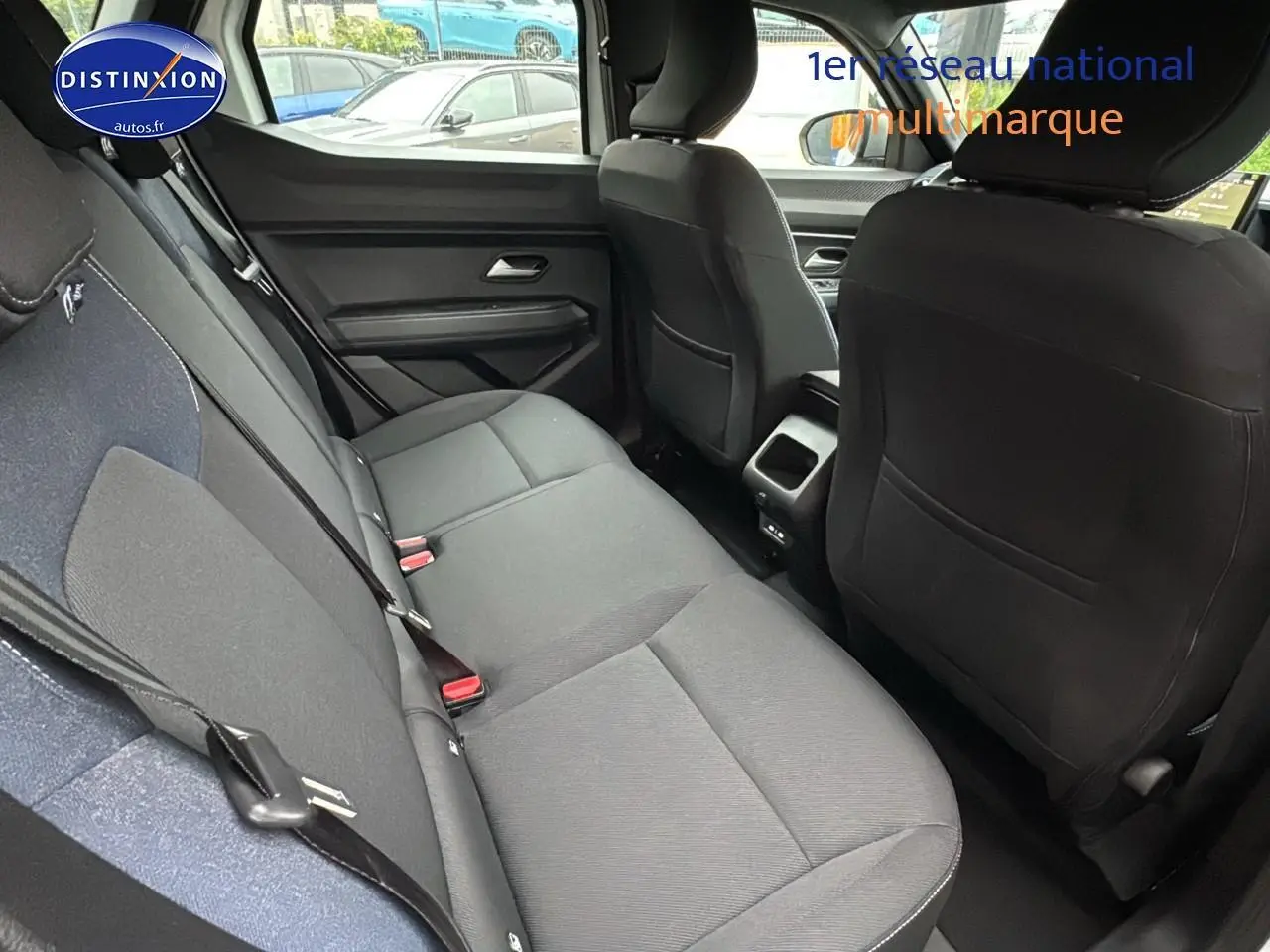 Vue intérieure arrière du Dacia Duster blanc Arctic 2025, sièges noirs en tissu avec ceintures de sécurité visibles.