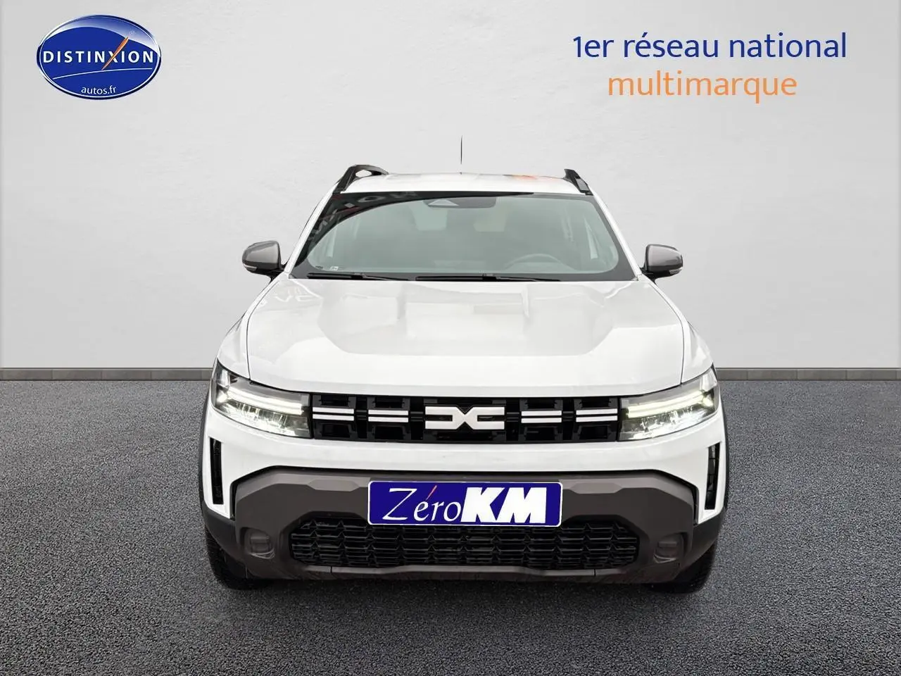 Vue frontale d'un Dacia Duster blanc arctic avec calandre noire et phares LED allumés sur fond neutre.