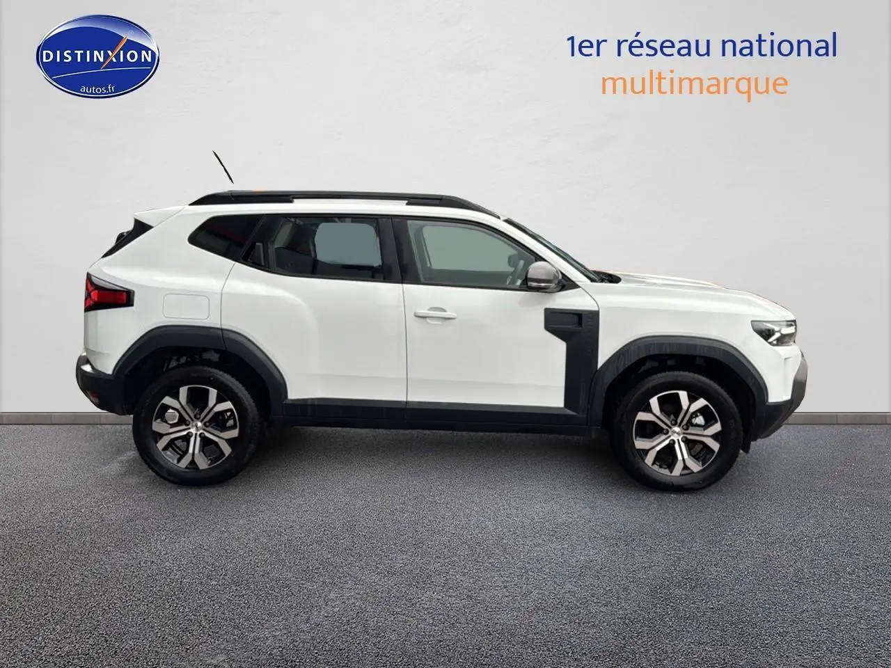 Profil droit du Dacia Duster blanc arctic 2025 avec jantes alu et barres de toit noires visibles.