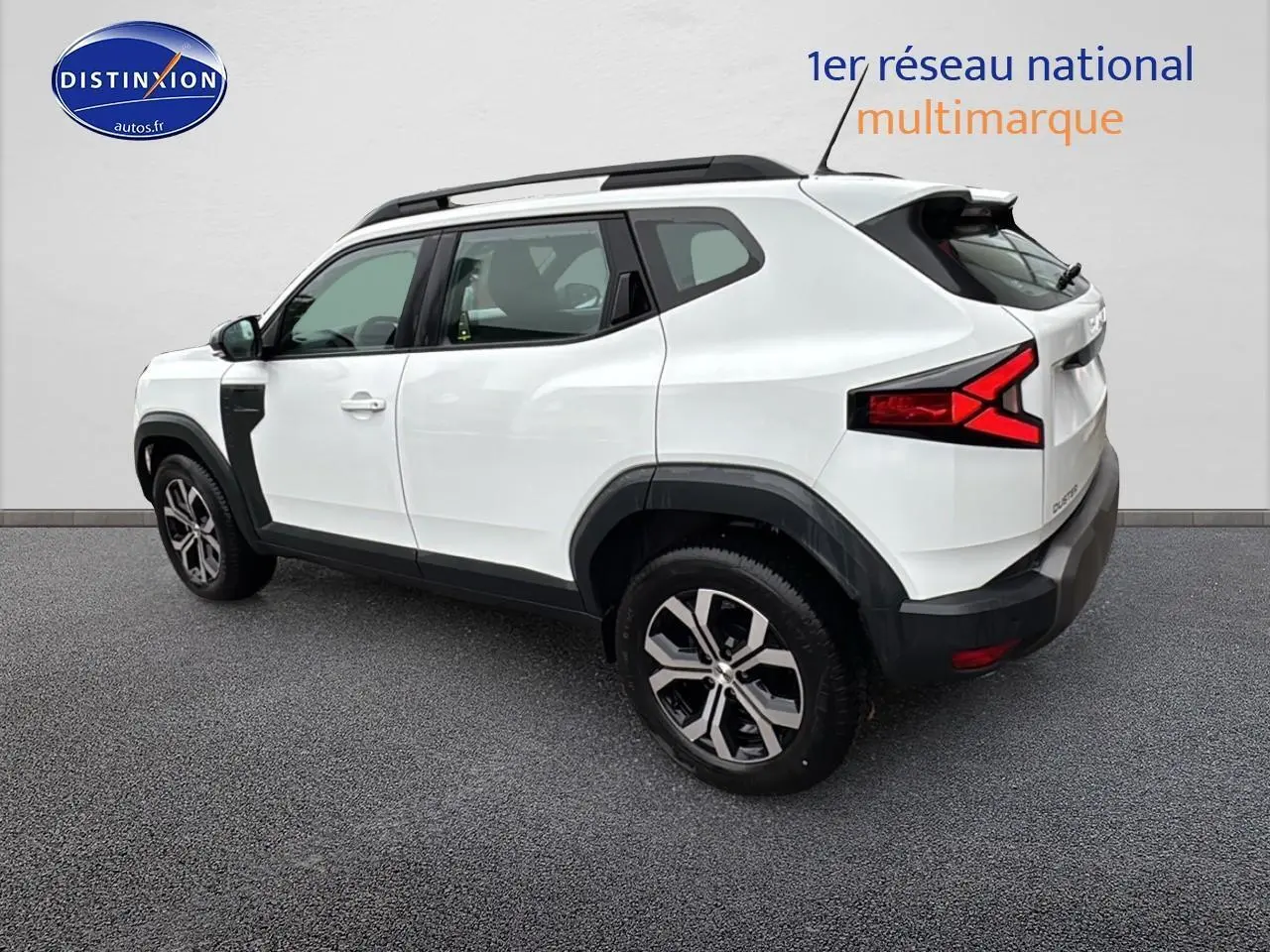 Vue 3/4 arrière droite du Dacia Duster blanc arctic 2025 avec jantes alu et barres de toit noires.