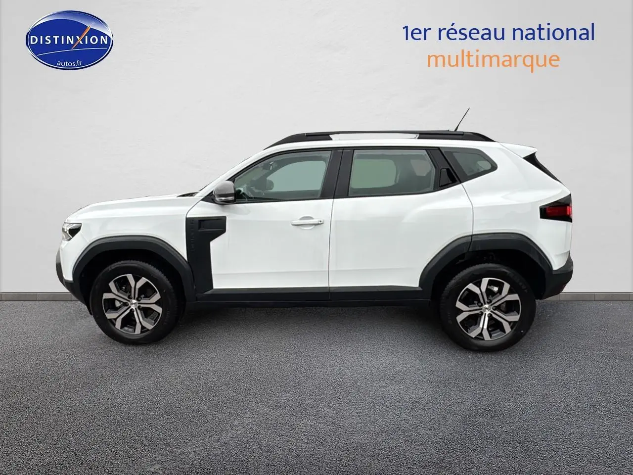 Profil côté gauche du Dacia Duster blanc Arctic 2025 avec jantes alu et barres de toit noires.