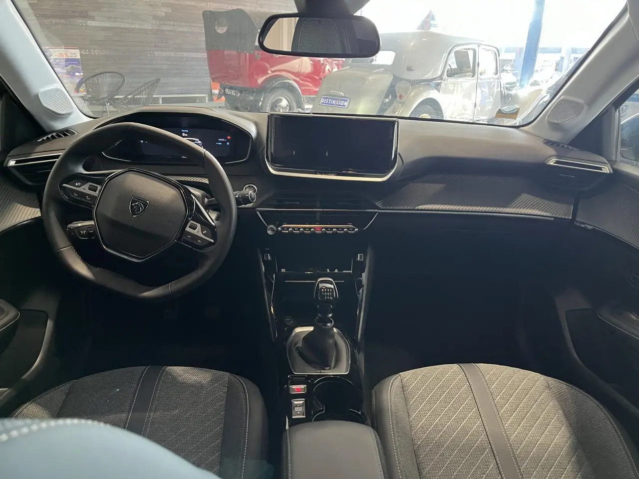 Intérieur Peugeot 208 2024 vu de face, volant cuir, tableau de bord numérique et levier de vitesse manuel.
