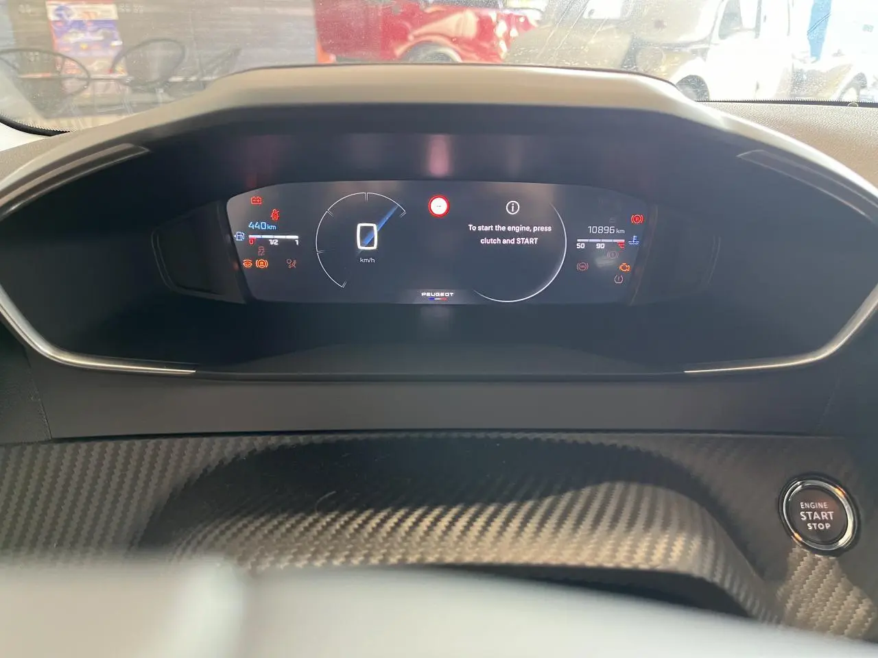 Vue rapprochée du tableau de bord numérique Peugeot 208 1.2 essence 2024 avec bouton start/stop et décor carbone.