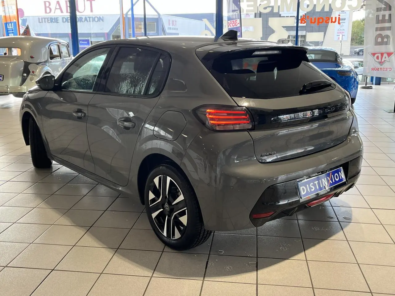 PEUGEOT 208 gris clair selenium vue 3/4 arrière droit en showroom avec jantes alliage bi-tons et feux LED allumés
