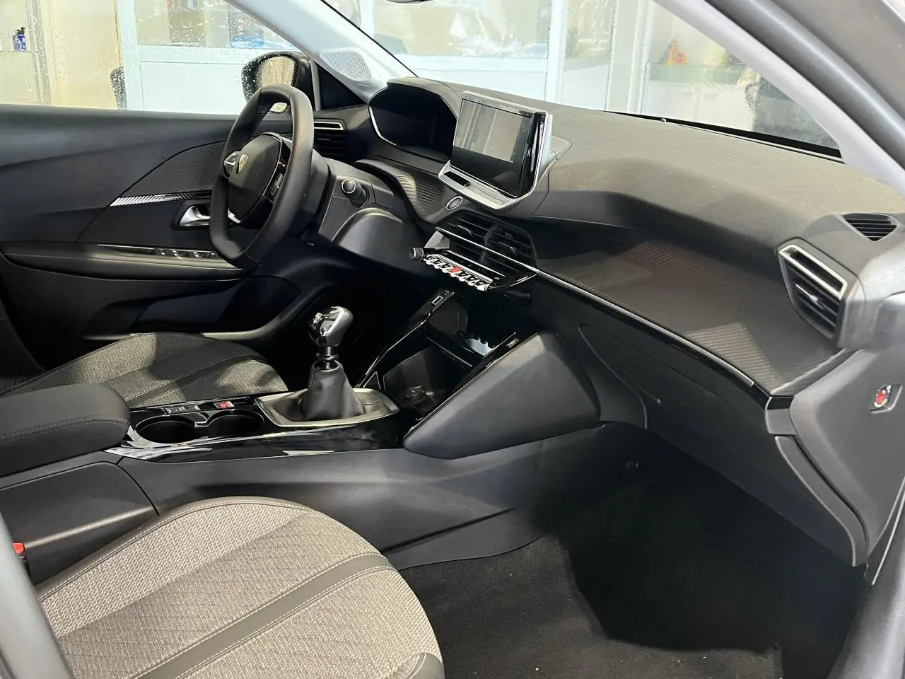 Intérieur avant droit de la Peugeot 208 2024 gris clair avec tableau de bord moderne et boîte manuelle.