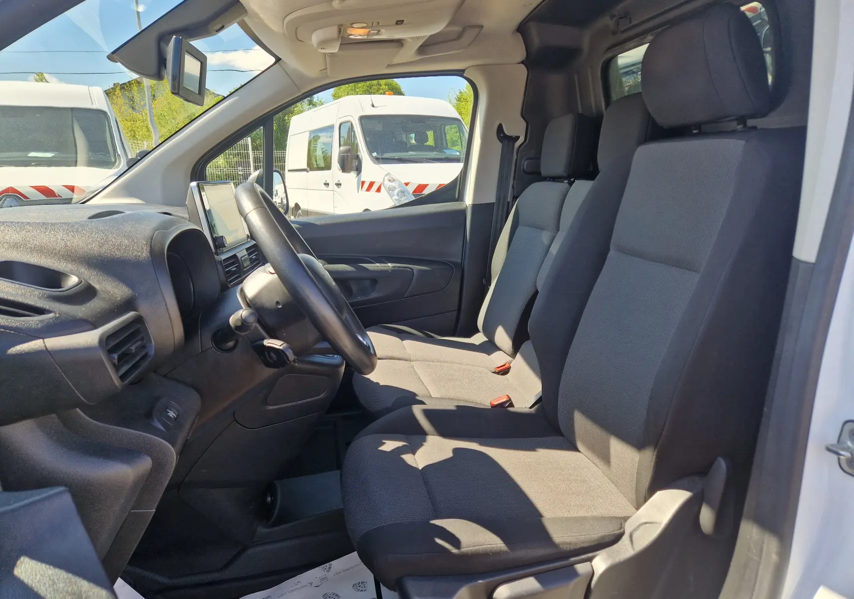 Vue intérieure côté conducteur du Citroën Berlingo blanc 2020, montrant les sièges tissu et le tableau de bord noir.