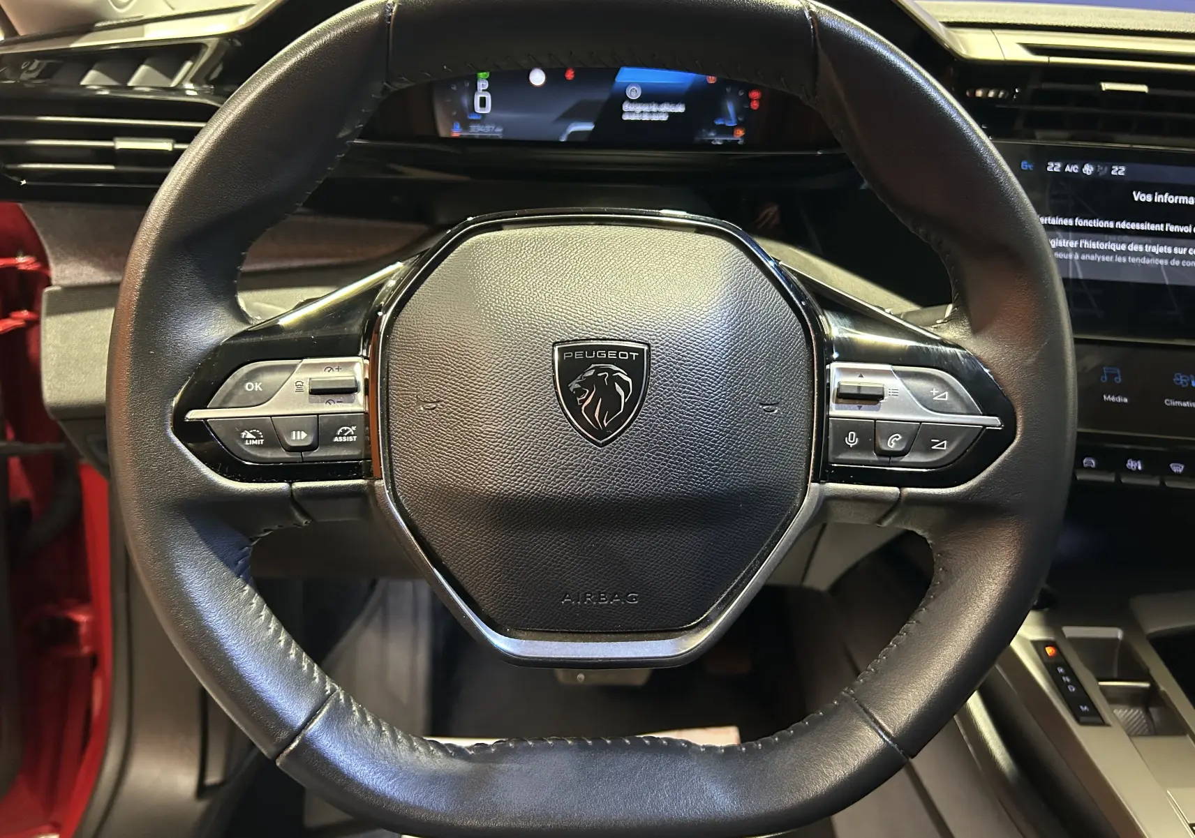 Vue rapprochée du volant cuir noir de la Peugeot 308 rouge 2024 avec commandes intégrées et tableau de bord numérique.