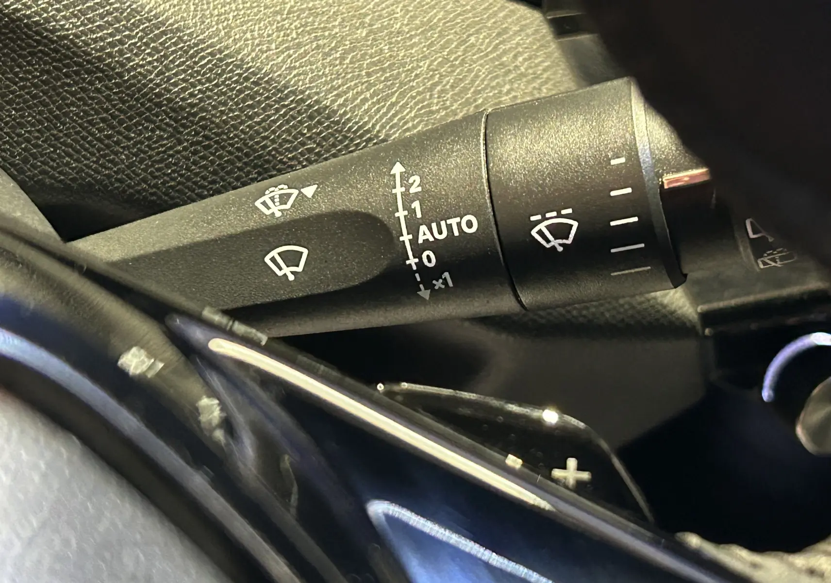 Gros plan sur la commande des essuie-glaces à gauche du volant dans l’habitacle du Peugeot 308 rouge 2024.