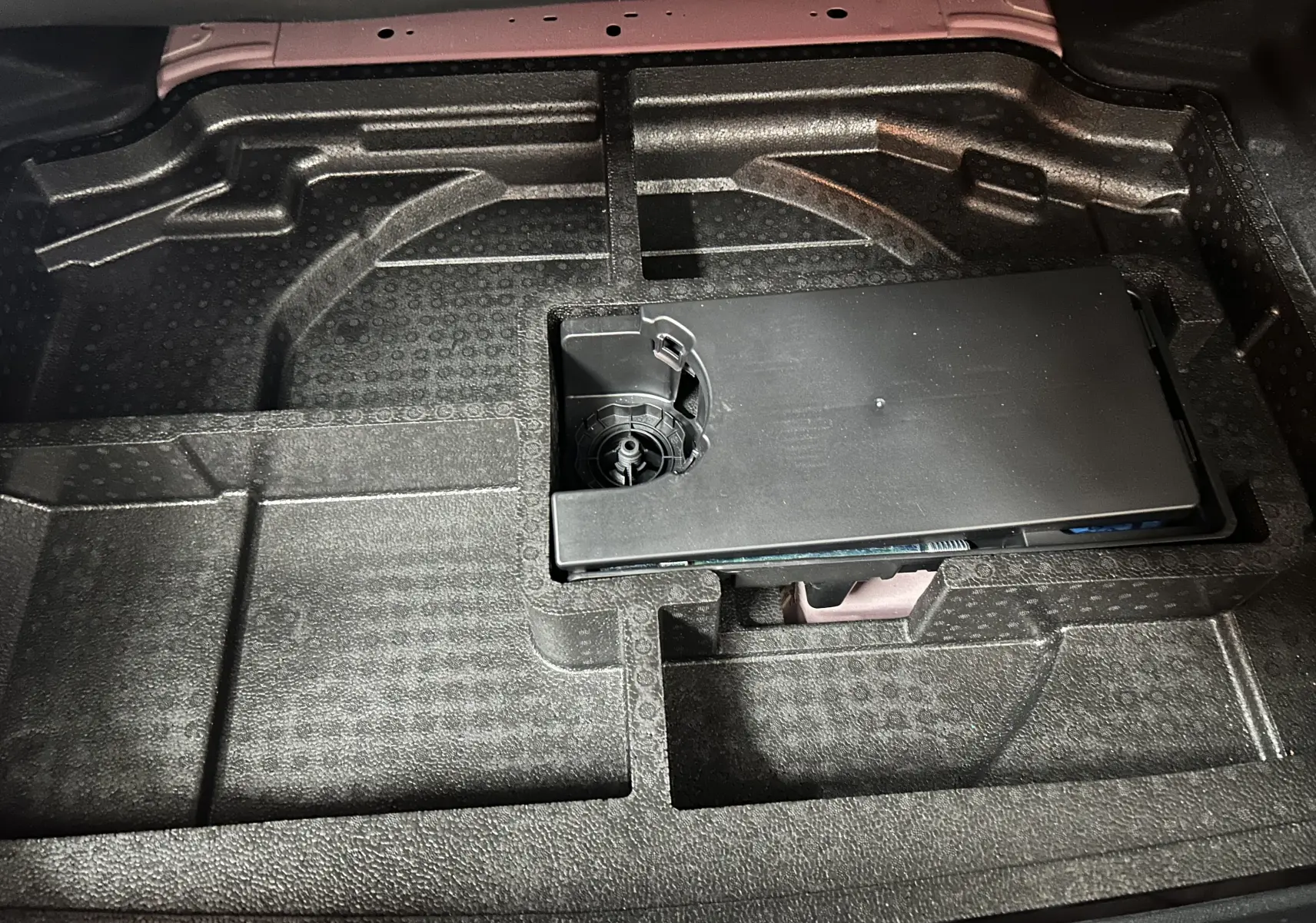 Vue rapprochée du compartiment de rangement sous le coffre d'une Peugeot 308 rouge, avec espace pour outils.