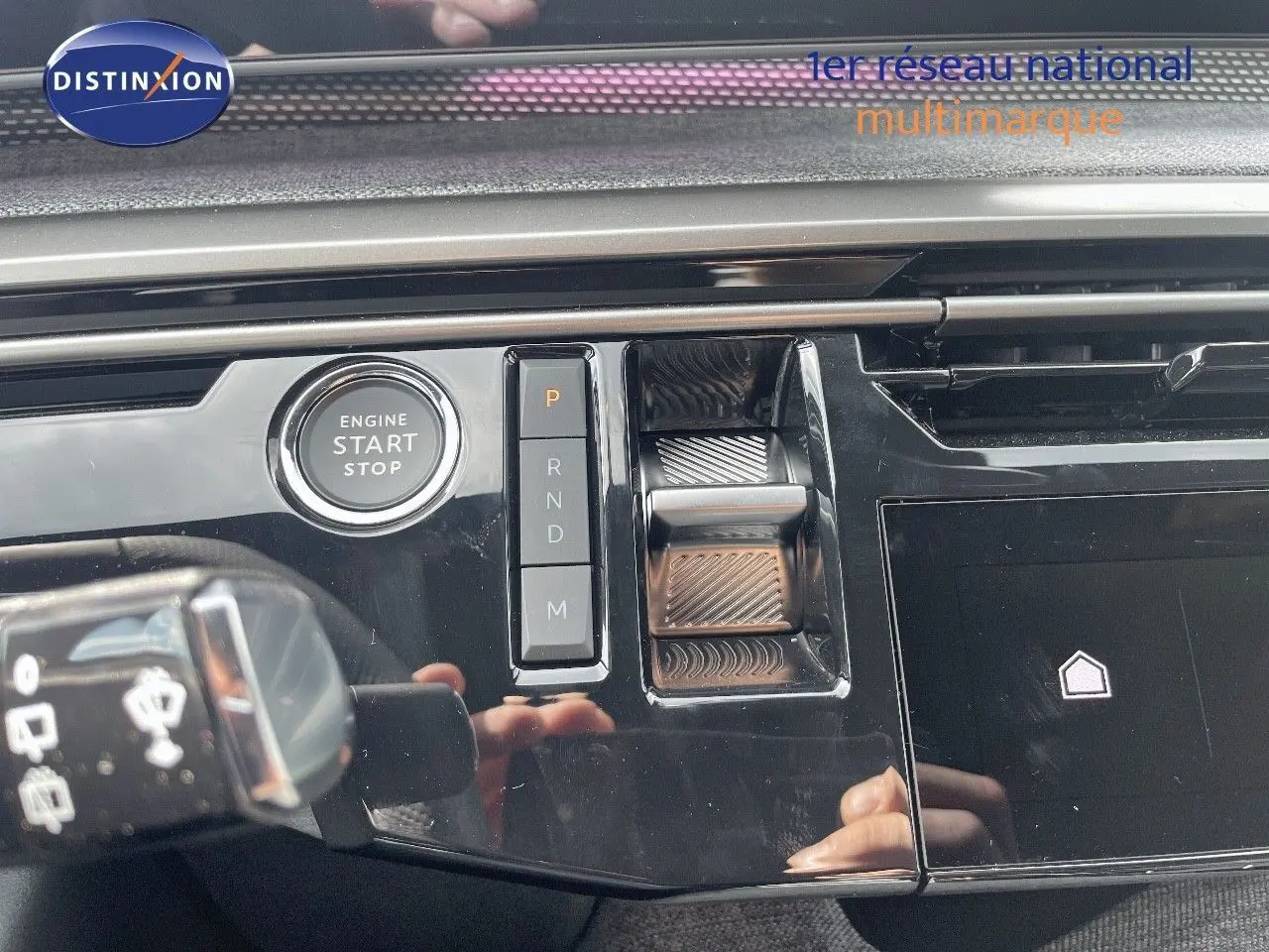 Gros plan sur la console centrale noire brillante du Peugeot 5008 Hybrid 2025 avec bouton start/stop et commandes de boîte automatique.