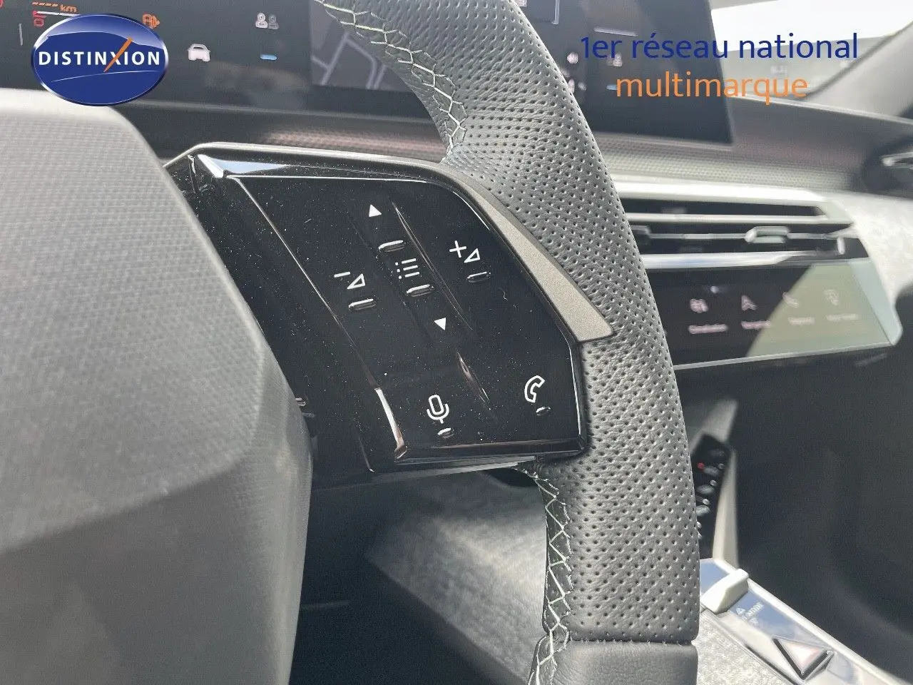 Gros plan sur les commandes gauche du volant perforé en cuir noir du Peugeot 5008 Hybrid 2025, avec tableau de bord en arrière-plan.