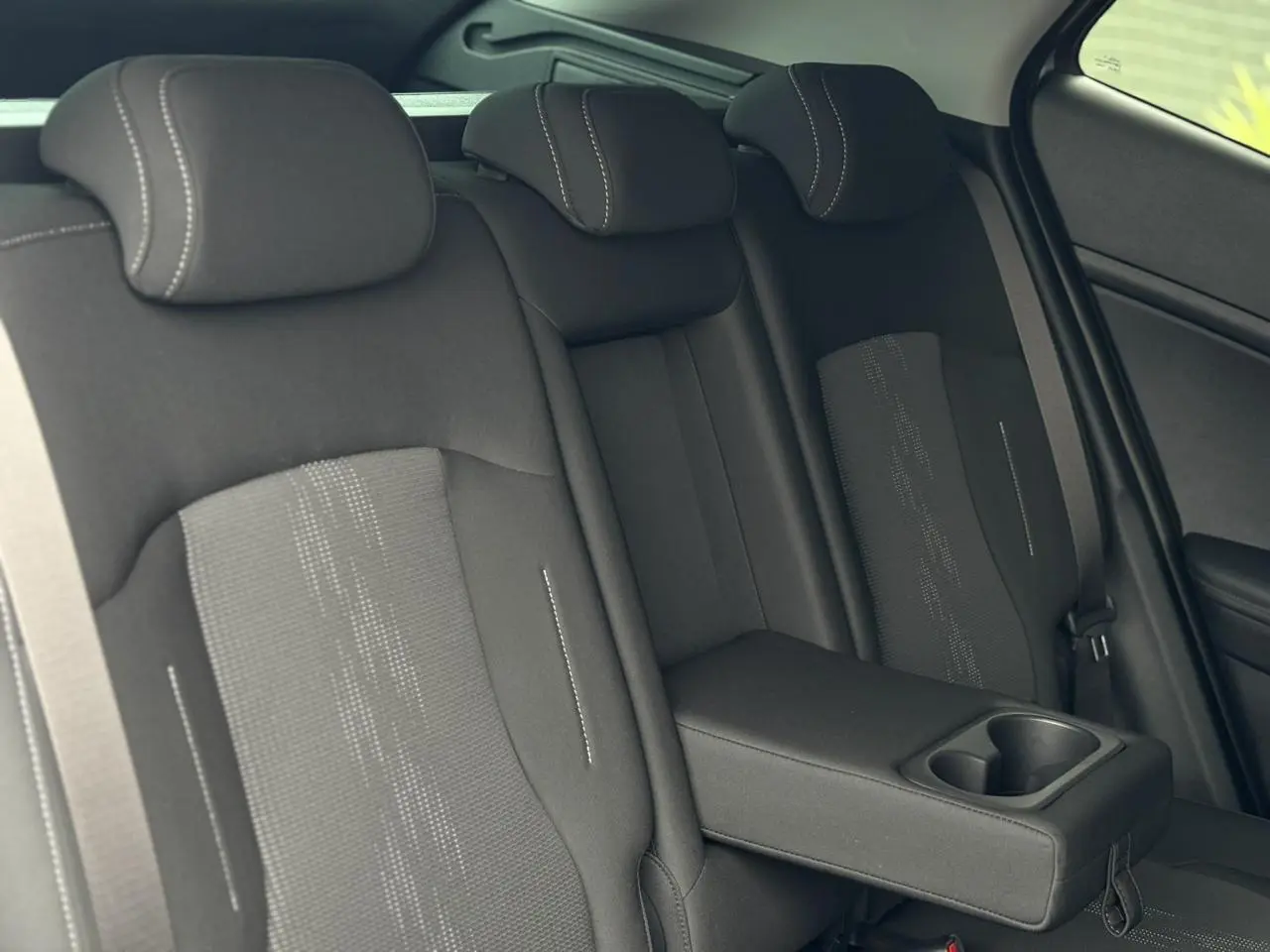 Vue latérale intérieure des sièges arrière noirs avec accoudoir central et porte-gobelets du Kia Sportage 2025.