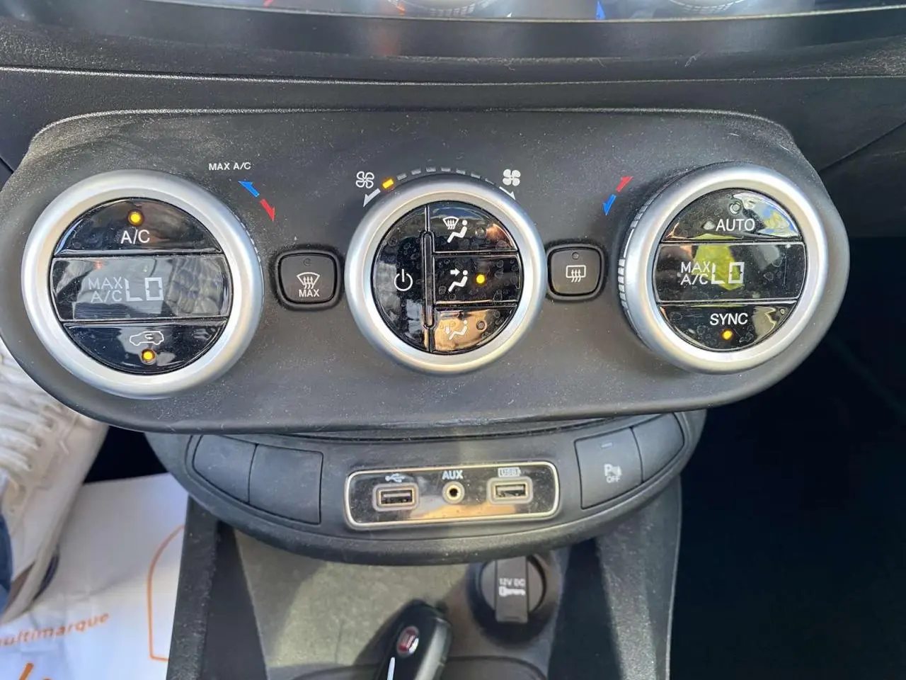 Gros plan sur les commandes de climatisation et les ports USB d'une Fiat 500X noire, version City Cross Business 2019.