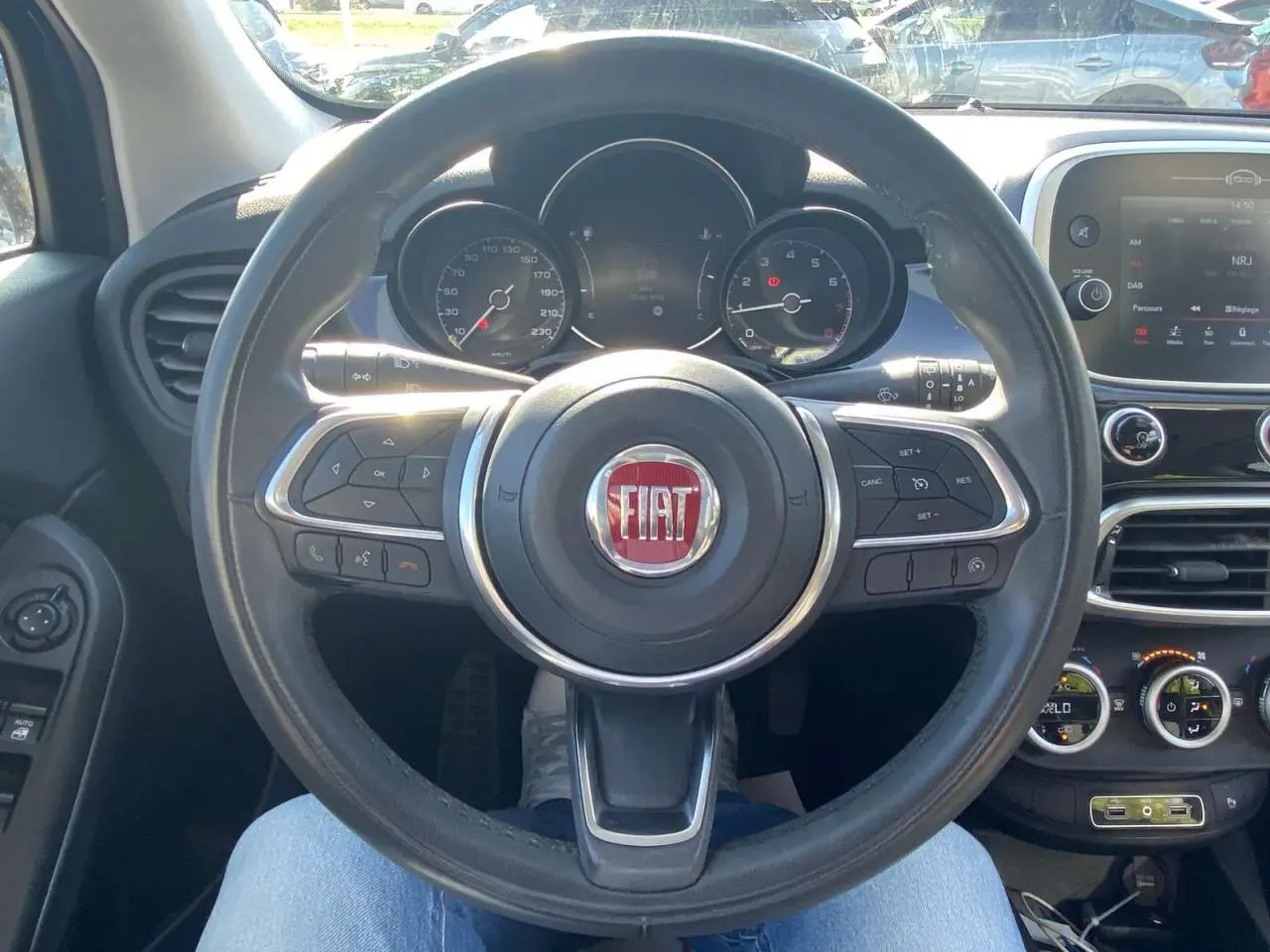 Vue intérieure centrée sur le volant du Fiat 500X noir, avec tableau de bord et écran multimédia visibles.