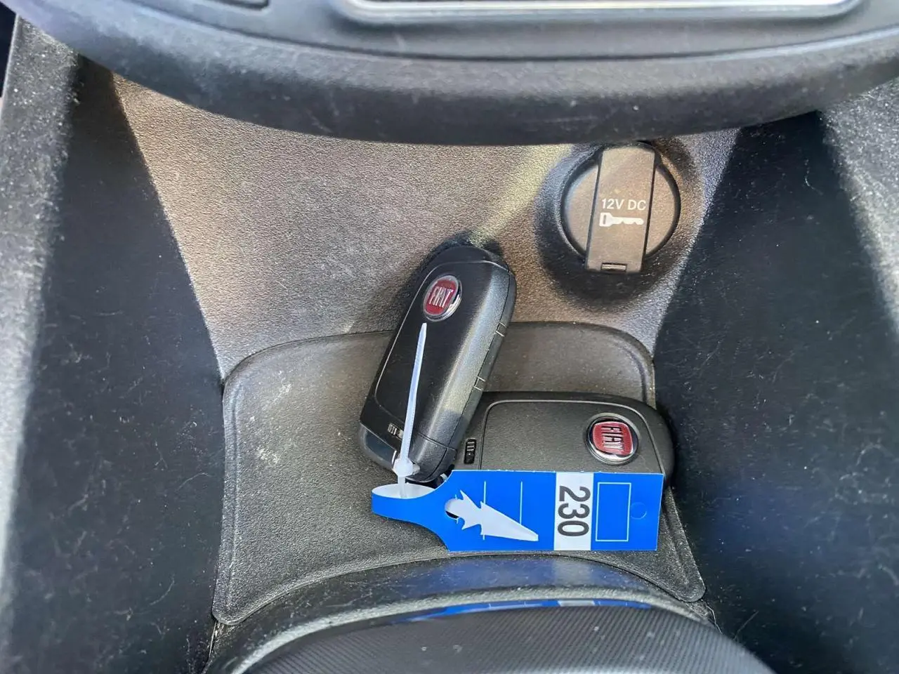 Gros plan sur deux clés FIAT posées dans le compartiment central noir avec prise 12V visible.