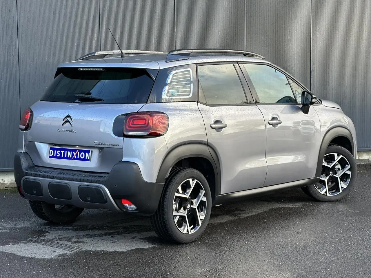 Vue 3/4 arrière droite d’un Citroën C3 Aircross gris Artense avec barres de toit et jantes alliage 17 pouces.