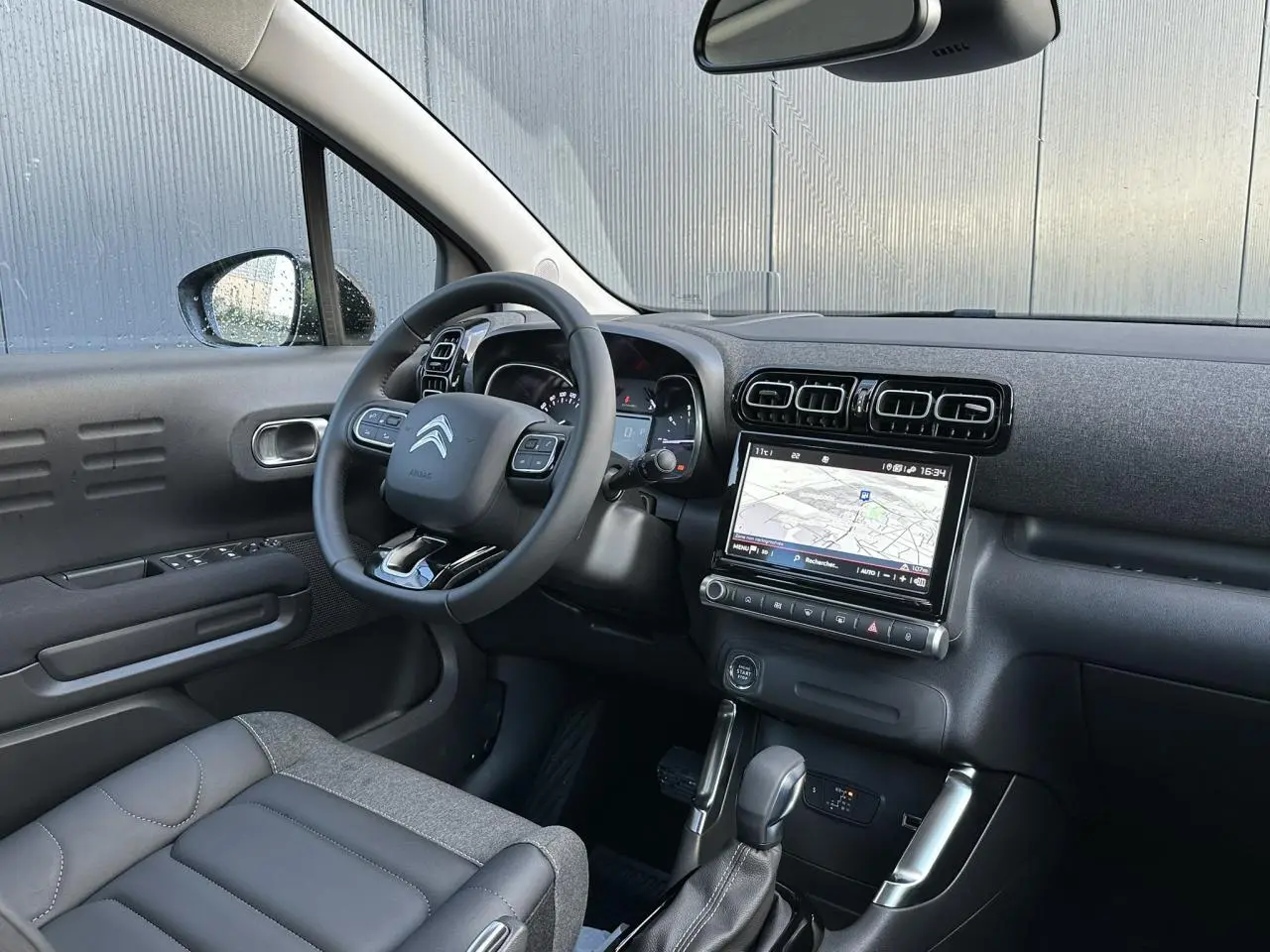 Vue intérieure côté conducteur du Citroën C3 Aircross 2024, montrant le volant, écran GPS tactile et sellerie gris foncé.