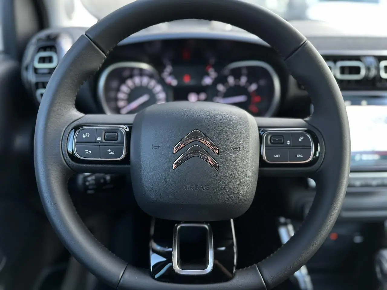 Gros plan sur le volant cuir noir du Citroën C3 Aircross 2024 avec commandes intégrées et tableau de bord flou en arrière-plan.