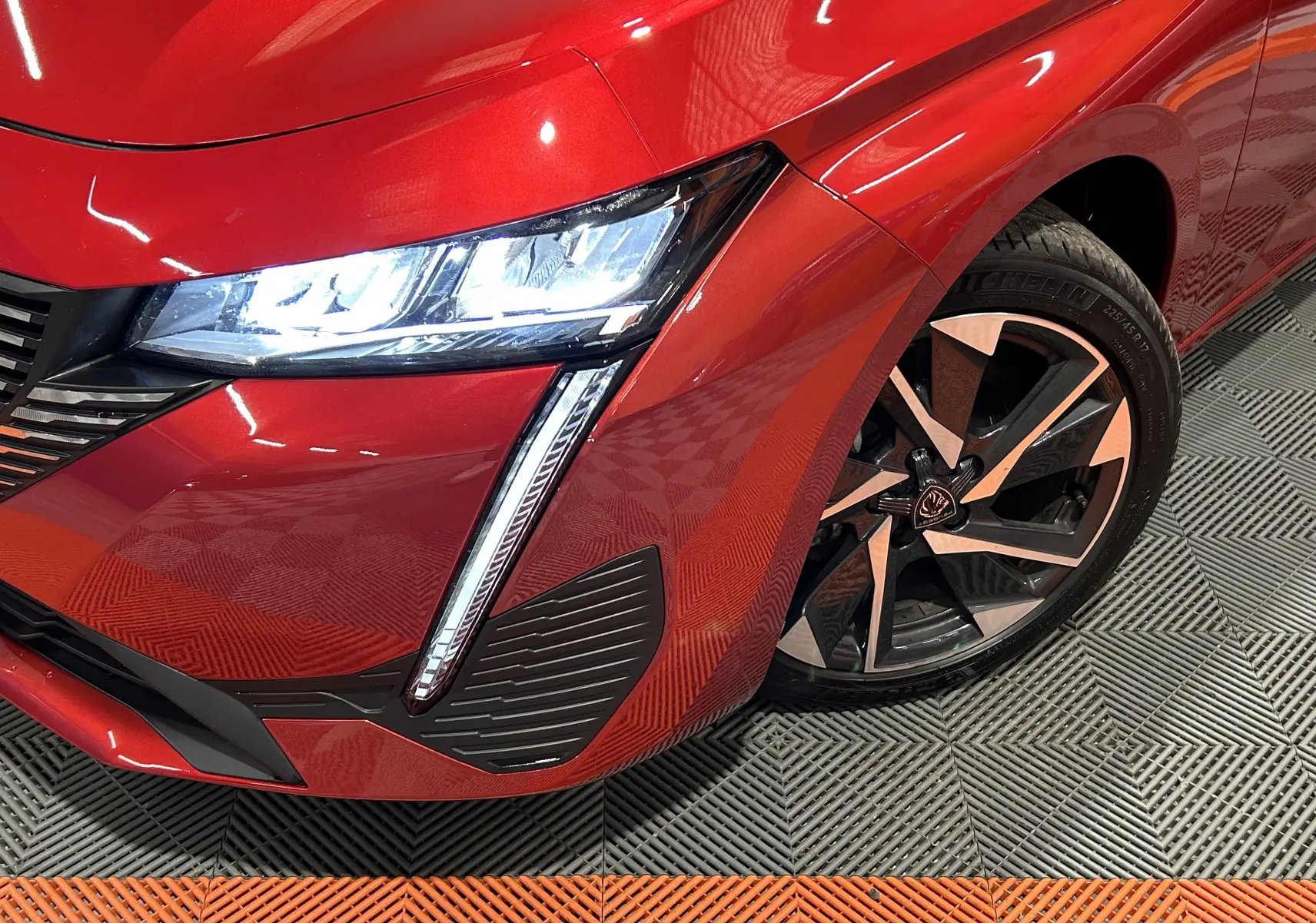 Gros plan sur l'avant droit rouge vif de la Peugeot 308 2024, mettant en valeur le phare LED et la jante alliage noire et argent.