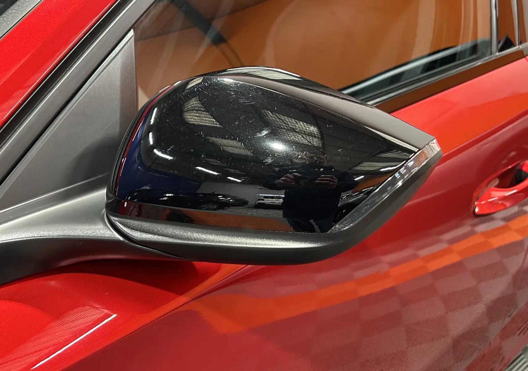 Rétroviseur noir en gros plan côté gauche sur Peugeot 308 rouge 2024, avec reflet de l'environnement intérieur.