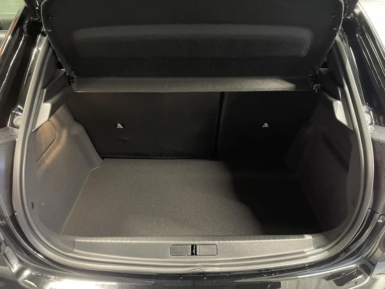 Coffre ouvert vu de l'arrière d'une Peugeot 208 noire métallisée, montrant un espace de chargement vide et propre.