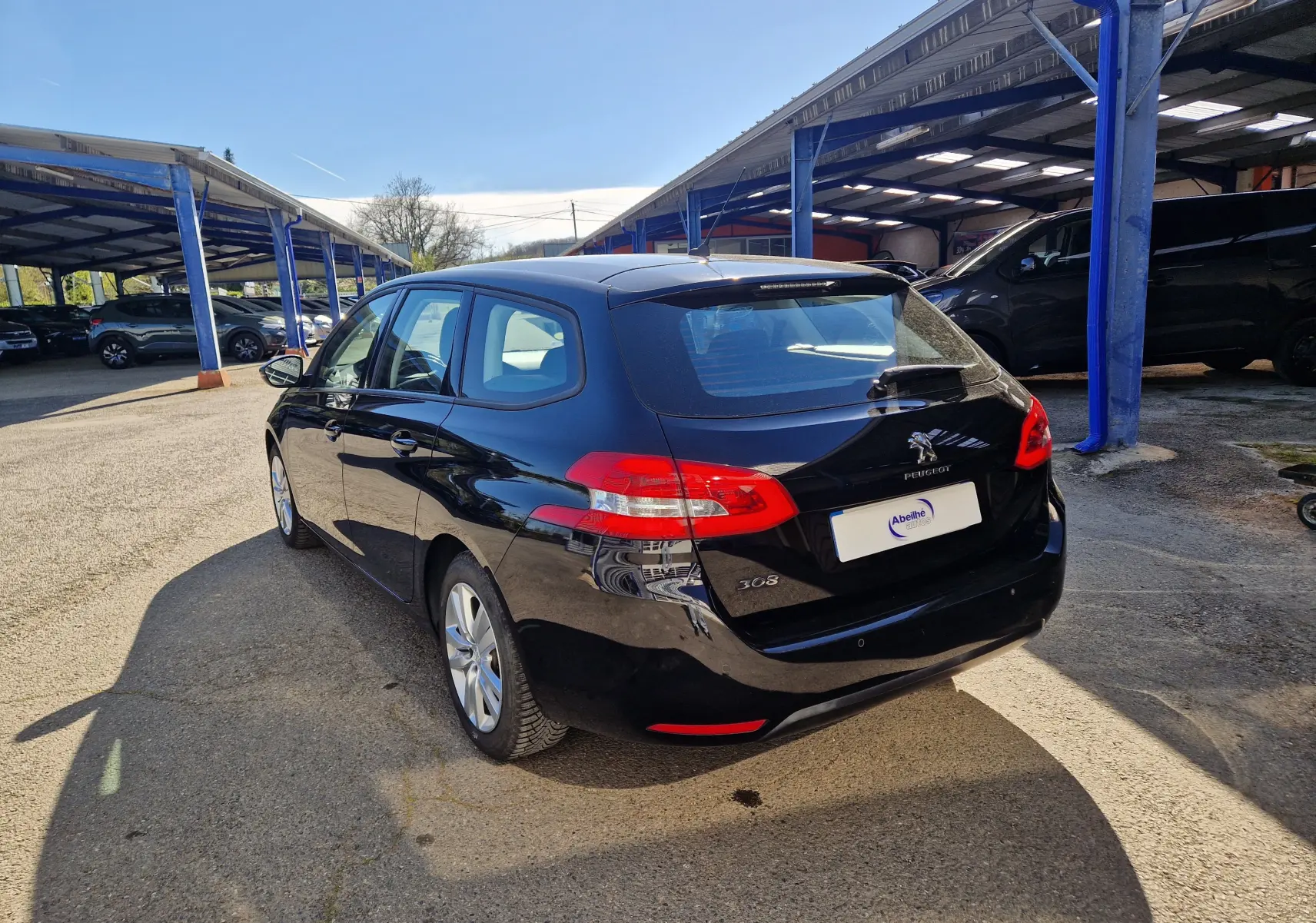 Vue 3/4 arrière droite d'une Peugeot 308 SW noire de 2021 stationnée sous un abri en extérieur.