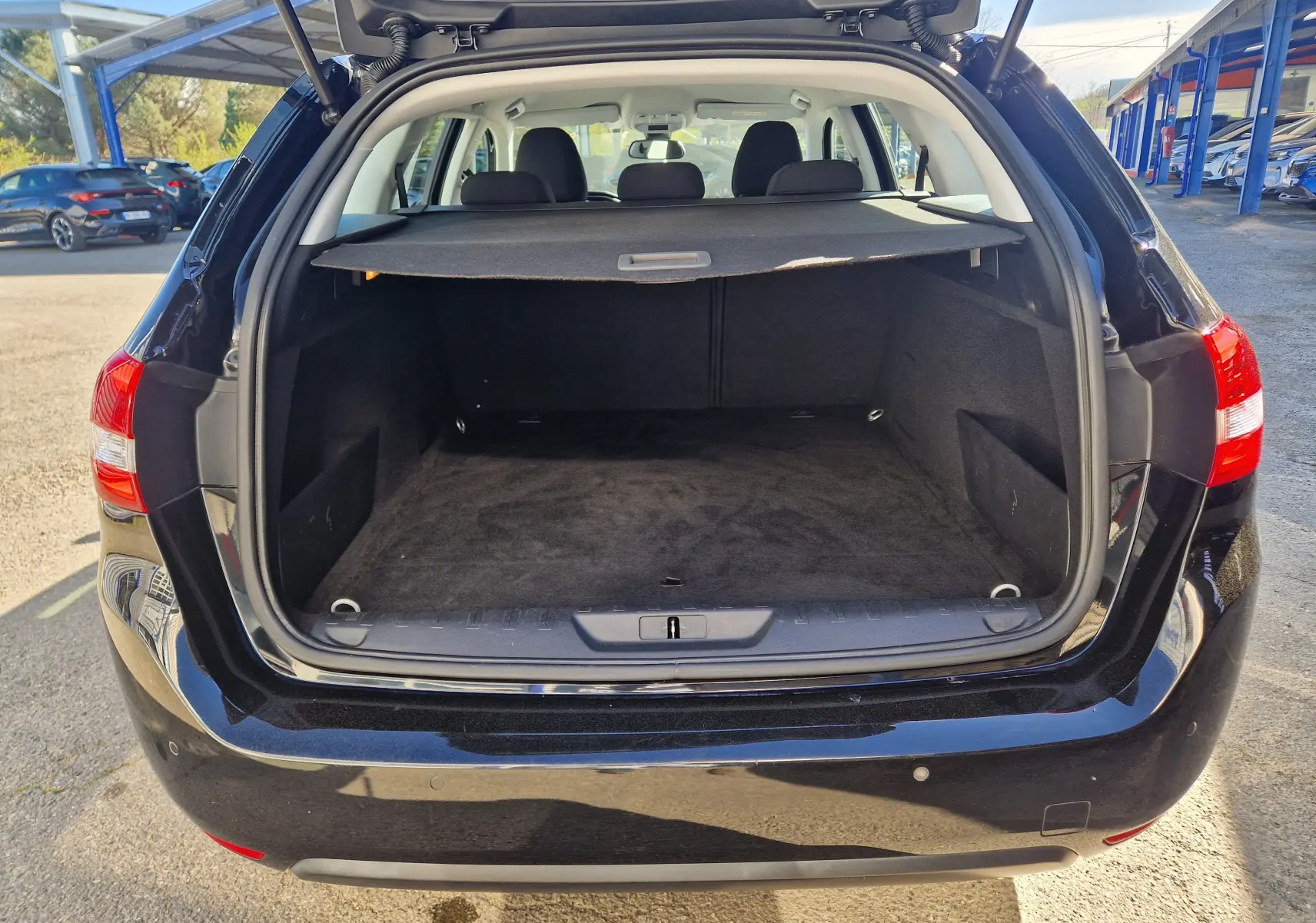 Vue arrière ouverte sur le coffre spacieux d’un Peugeot 308 SW noir, avec cache-bagages et intérieur sombre visible.