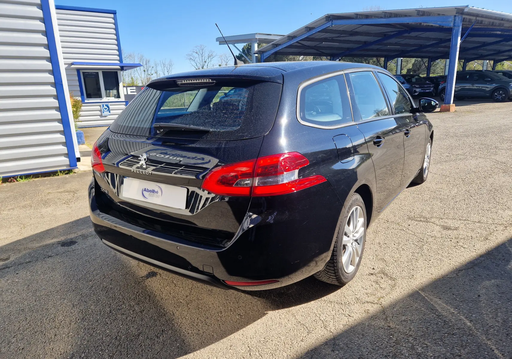 Vue 3/4 arrière droite d'une Peugeot 308 SW noire 2021, break diesel avec feux arrière rouges et jantes alliage.