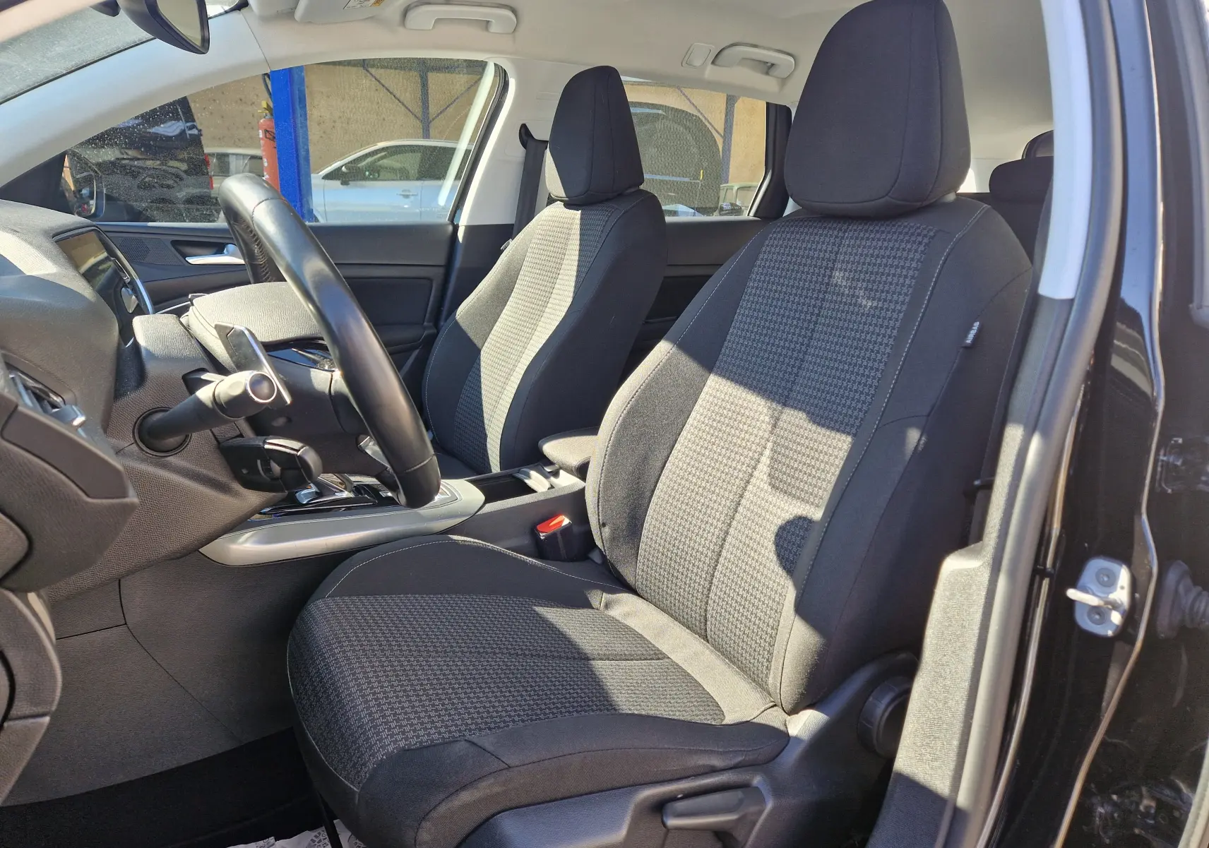 Vue intérieure côté conducteur de la Peugeot 308 SW noire, montrant les sièges avant en tissu et le volant.