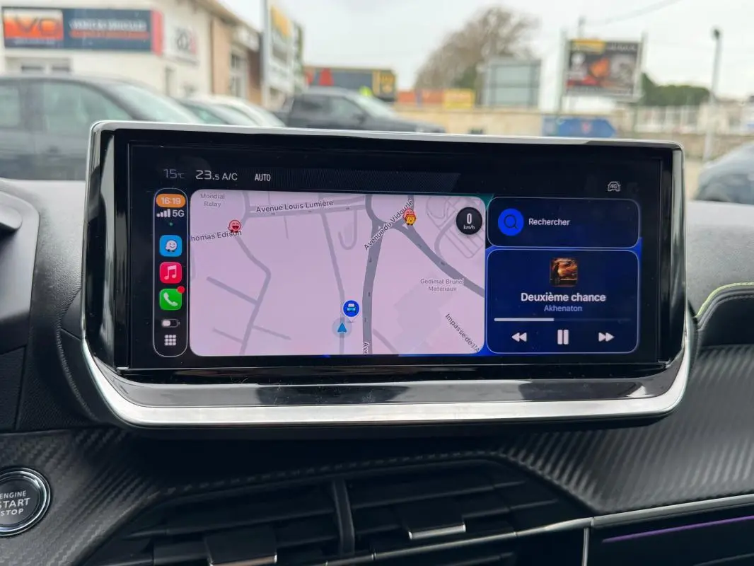 Vue rapprochée de l’écran tactile central du Peugeot 208 gris, affichant la navigation et la musique en cours.