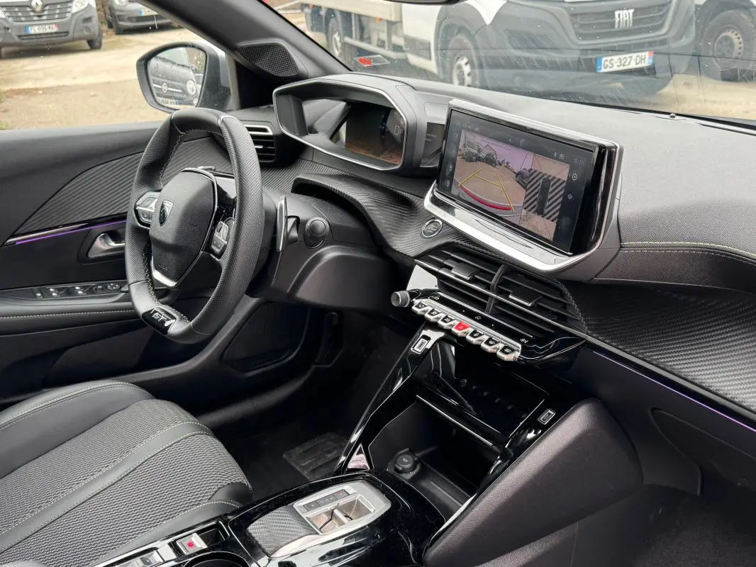 Vue intérieure côté conducteur de la Peugeot 208 Hybrid 110 e-DCS6 GT 2025, avec écran tactile et volant compact noir.