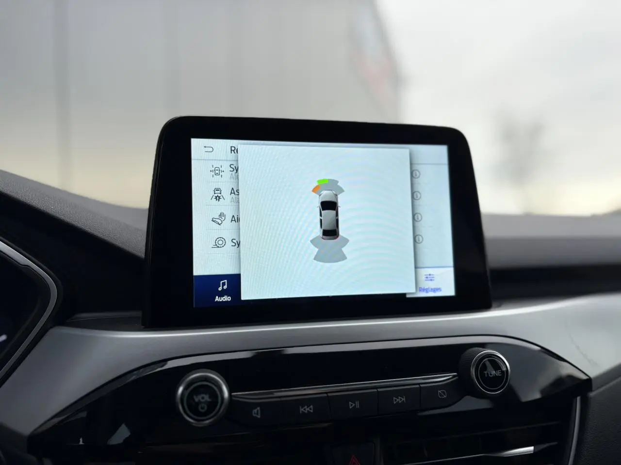 Écran tactile central du Ford Kuga 2024 affichant l'aide au stationnement avec interface moderne et commandes audio intégrées.