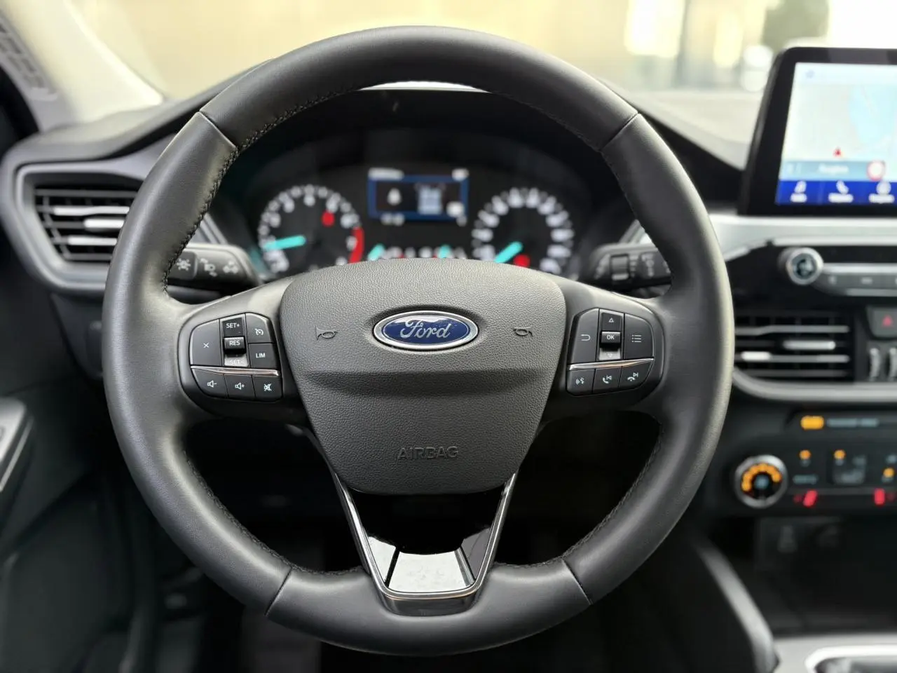 Volant multifonctions en cuir noir au centre du tableau de bord du Ford Kuga 2024 avec écran tactile GPS en arrière-plan.