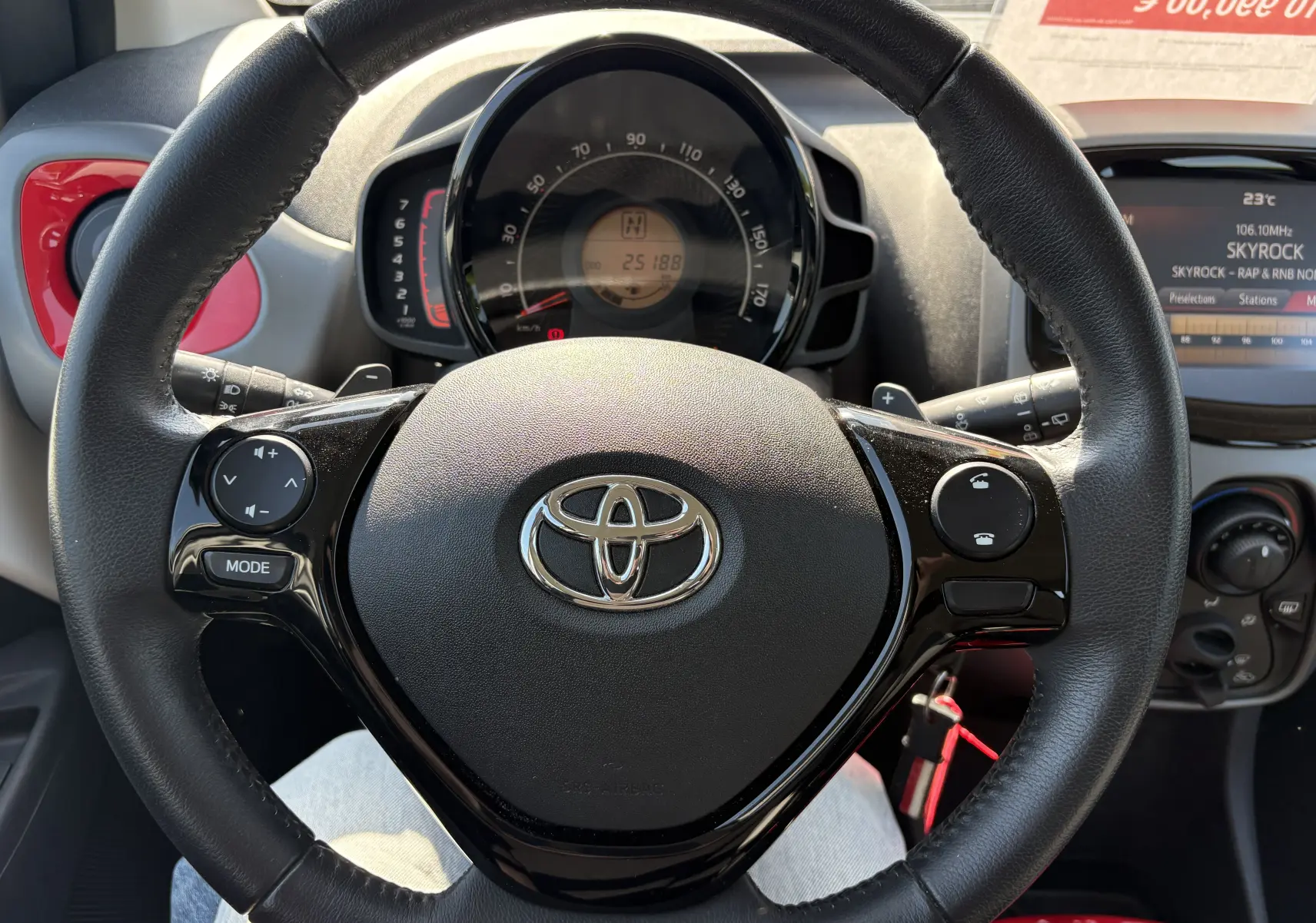 Vue intérieure centrée sur le volant noir de la Toyota Aygo MC 2020 avec commandes audio et tableau de bord visible.