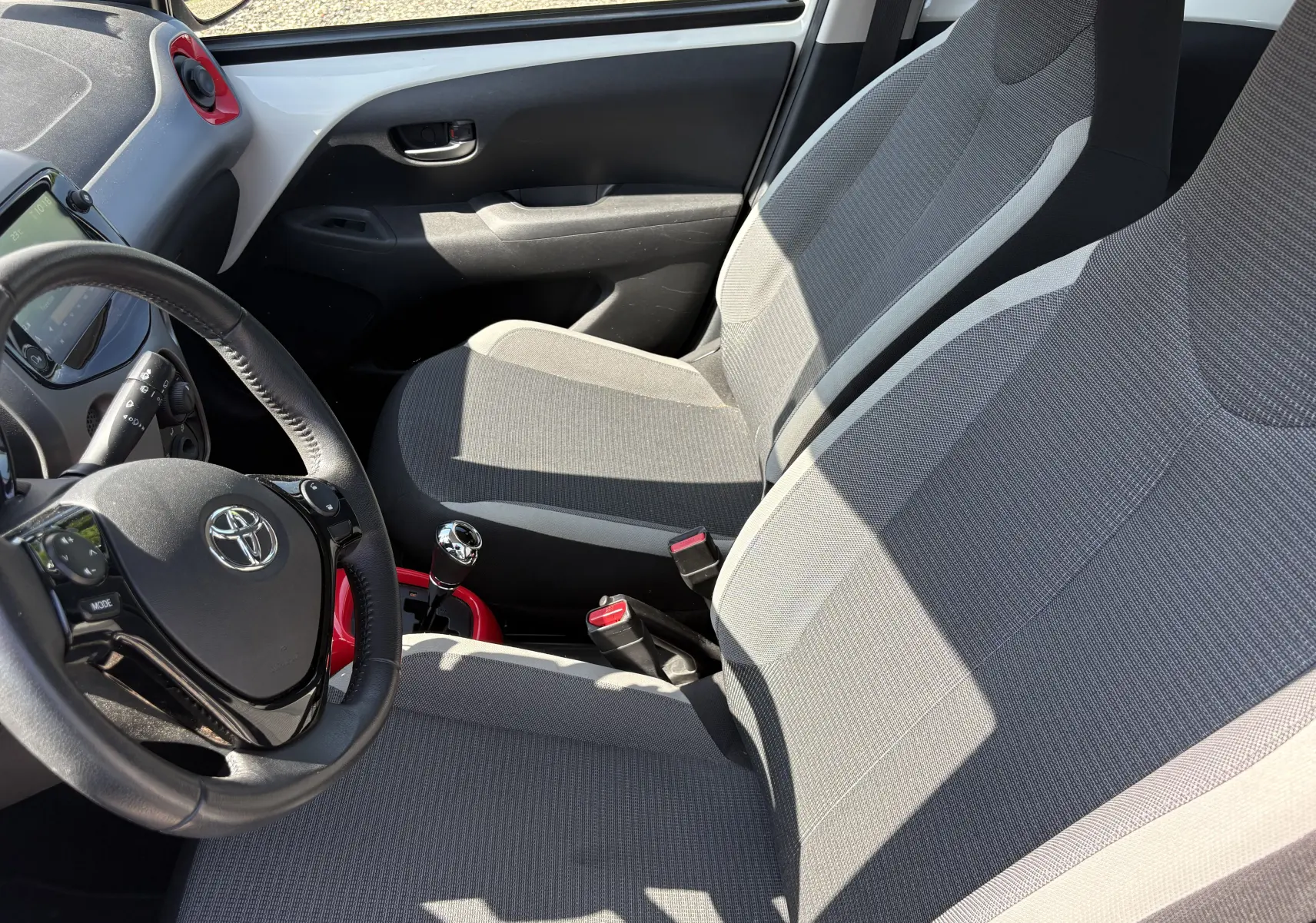 Vue intérieure côté conducteur de la Toyota Aygo MC 2020, sièges gris et volant avec commandes intégrées.