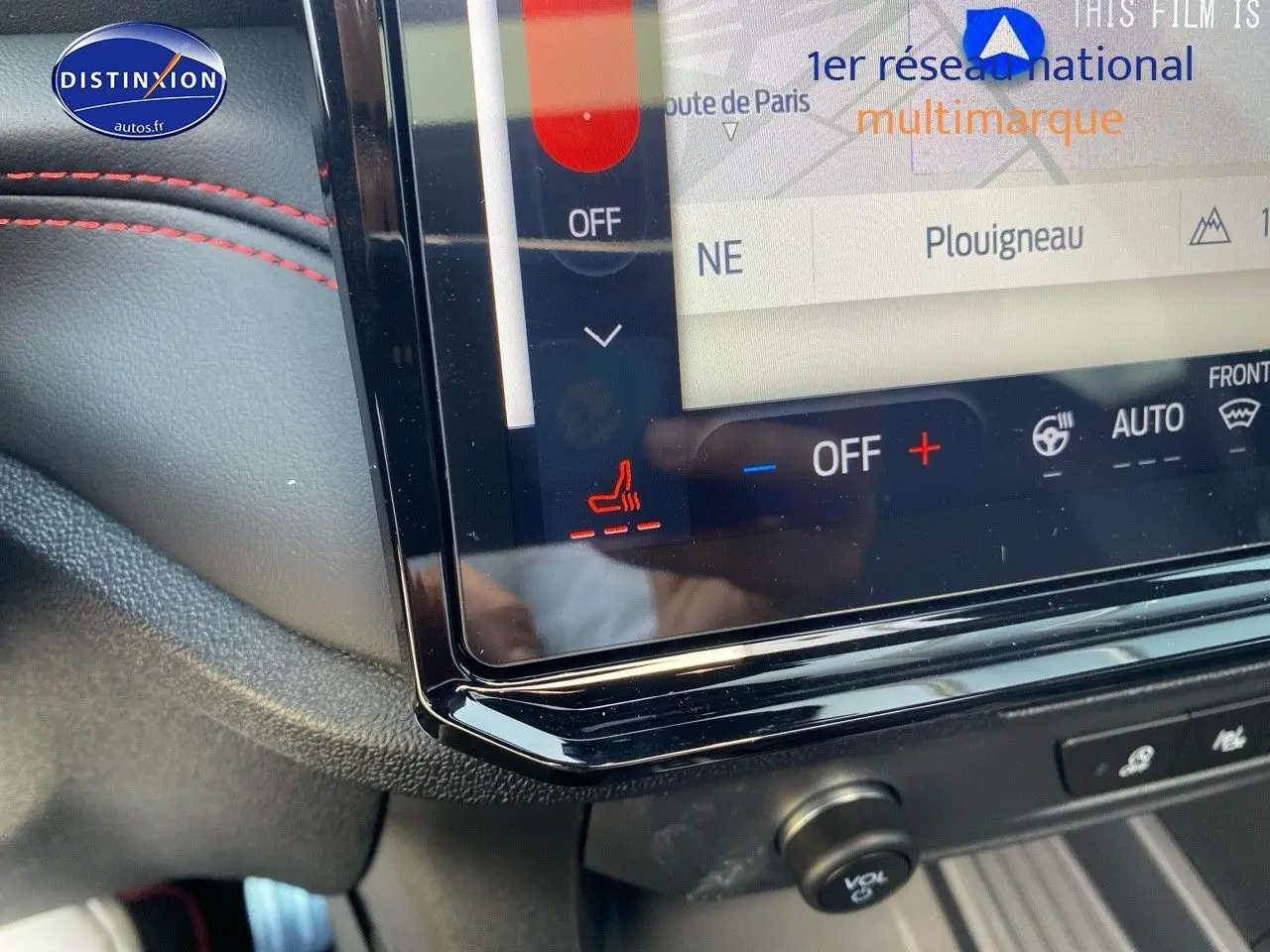 Détail de l'écran tactile central avec commandes de climatisation et surpiqûres rouges sur tableau de bord noir du Ford Puma rouge.