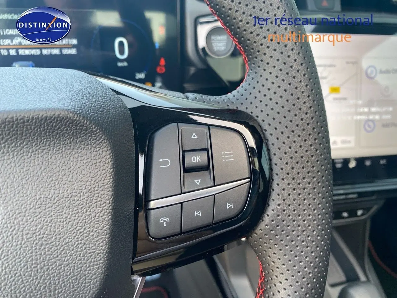 Gros plan sur les commandes au volant perforé avec surpiqûres rouges du Ford Puma rouge, tableau de bord et écran tactile en arrière-plan.