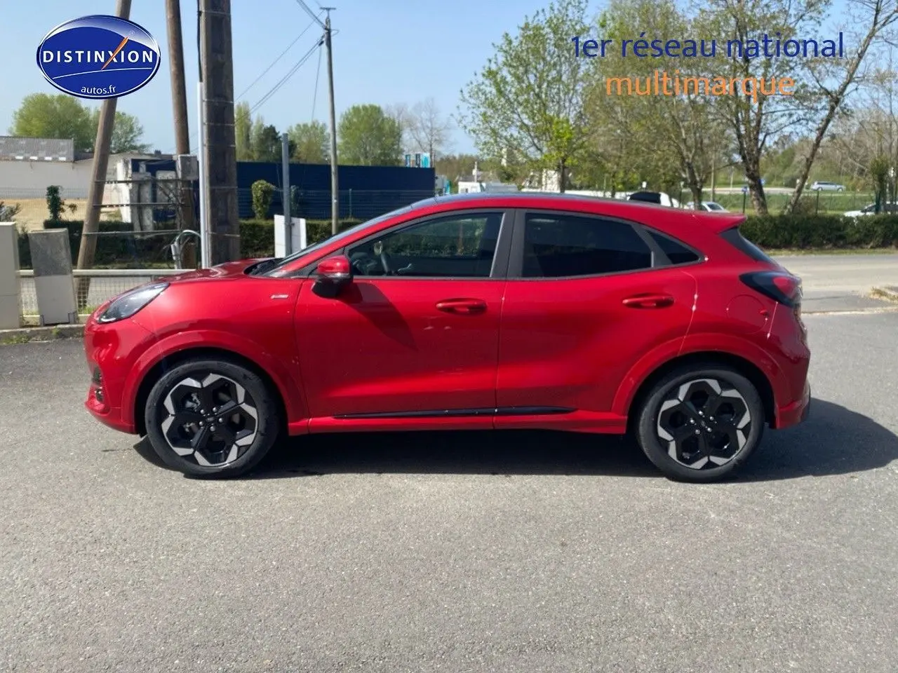 Profil côté gauche d'un Ford Puma rouge métallisé avec jantes alu noires au design hexagonal, stationné en extérieur.