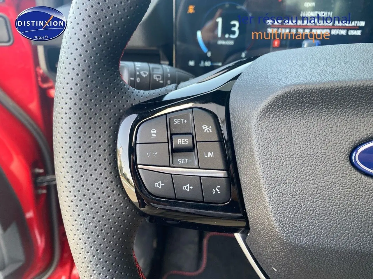 Gros plan sur les commandes au volant perforé avec surpiqûres rouges du Ford Puma rouge métallisé.