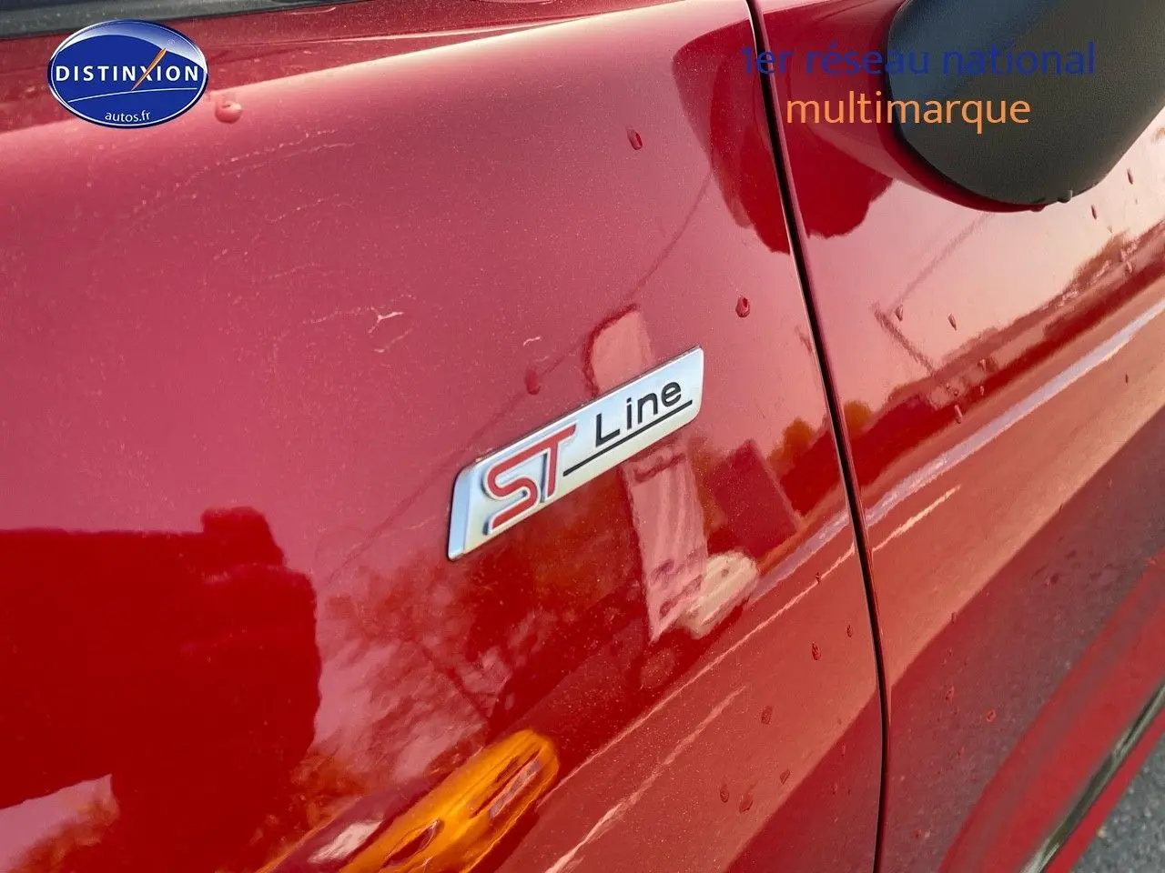 Gros plan sur l’écusson ST-Line côté gauche d’un Ford Puma rouge métallisé avec gouttes d’eau visibles.