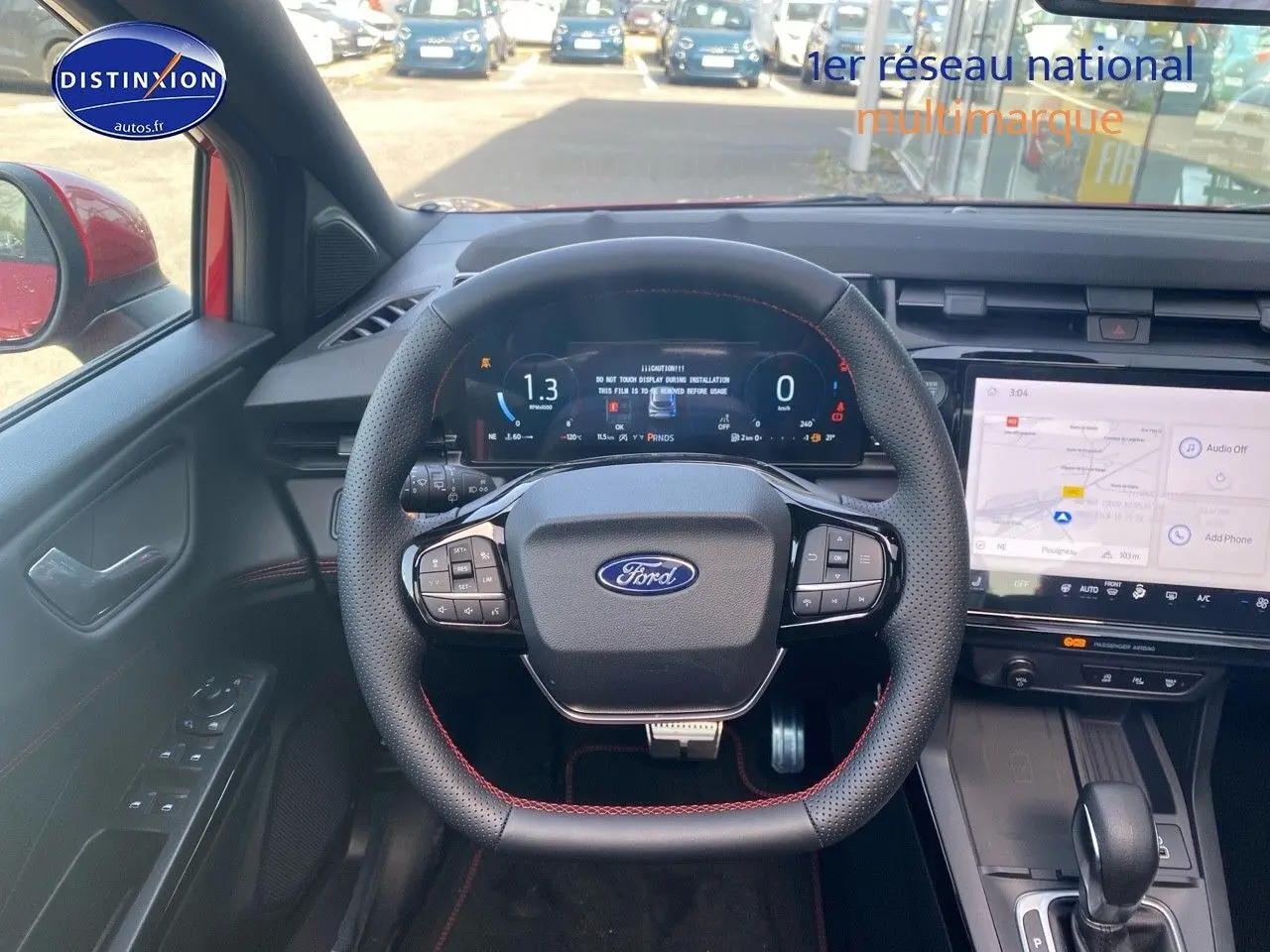 Vue intérieure centrée sur le volant noir avec surpiqûres rouges du Ford Puma rouge, écran tactile et tableau de bord numérique.