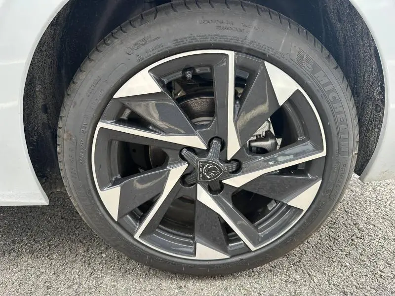 Gros plan sur la jante alu noire et argentée du côté gauche d'une Peugeot 308 blanche Okénite.
