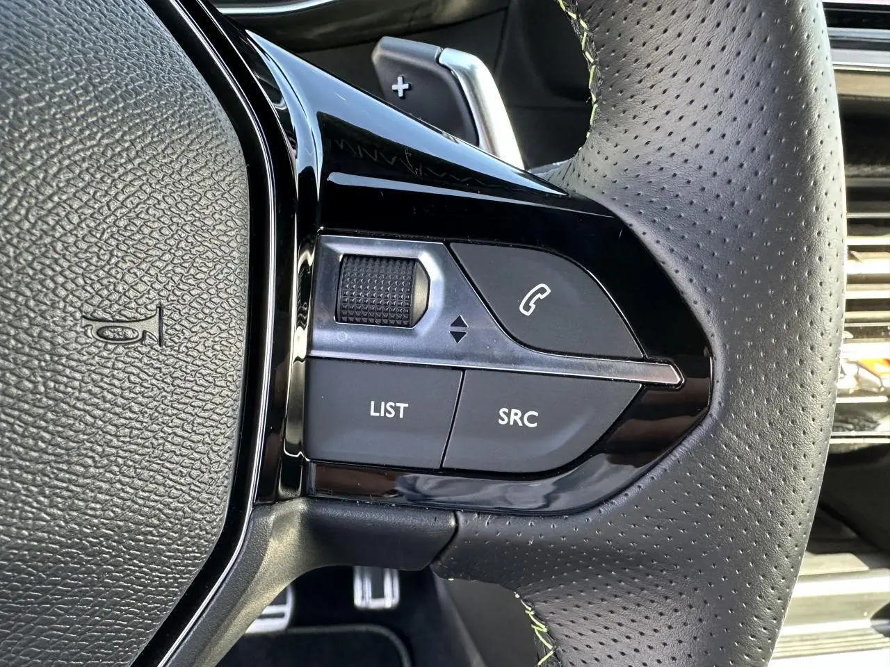 Gros plan sur les commandes gauche du volant cuir perforé gris du Peugeot 208 Hybrid 145 e-DSC6 GT 2024.